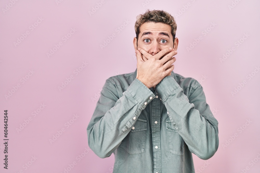 Hispanic man with beard standing over pink background shocked covering mouth with hands for mistake. secret concept. Hispanic man with beard standing over pink background shocked covering mouth with hands for mistake. secret concept.