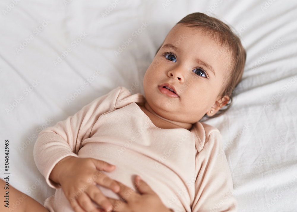 Adorable hispanic baby lying on bed with relaxed expression at bedroom Adorable hispanic baby lying on bed with relaxed expression at bedroom
