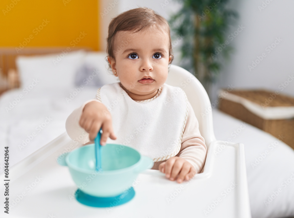 Adorable hispanic baby holding spoon sitting on highchair at bedroom Adorable hispanic baby holding spoon sitting on highchair at bedroom