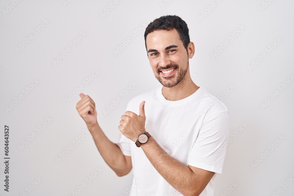 Handsome hispanic man standing over white background pointing to the back behind with hand and thumbs up, smiling confident