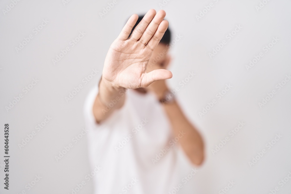 Obraz premium Handsome hispanic man standing over white background covering eyes with hands and doing stop gesture with sad and fear expression. embarrassed and negative concept.