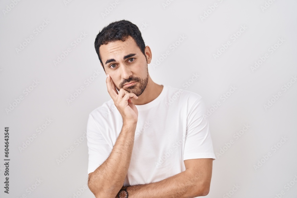 Handsome hispanic man standing over white background thinking looking tired and bored with depression problems with crossed arms. Handsome hispanic man standing over white background thinking looking tired and bored with depression problems with crossed arms.