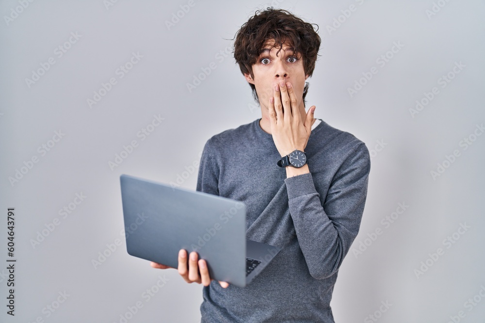 Young man working using computer laptop covering mouth with hand, shocked and afraid for mistake. surprised expression Young man working using computer laptop covering mouth with hand, shocked and afraid for mistake. surprised expression