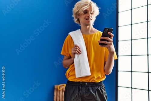 Young blond man smiling confident using smartphone at sport center