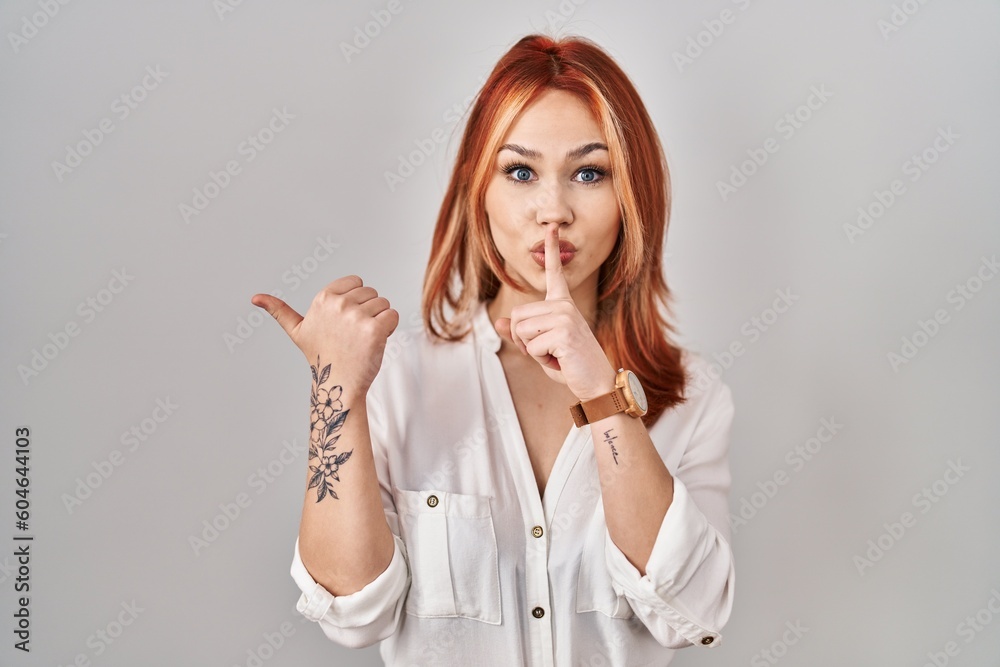 Young caucasian woman standing over isolated background asking to be quiet with finger on lips pointing with hand to the side. silence and secret concept. Young caucasian woman standing over isolated background asking to be quiet with finger on lips pointing with hand to the side. silence and secret concept.