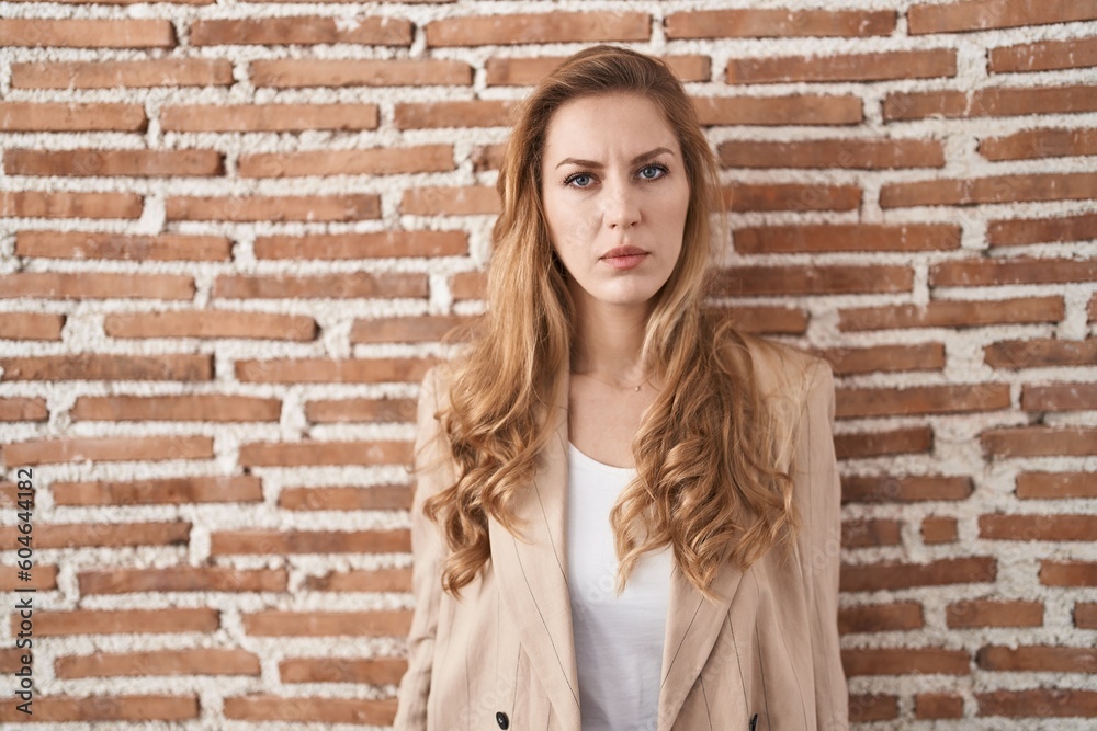 Beautiful blonde woman standing over bricks wall relaxed with serious expression on face. simple and natural looking at the camera.