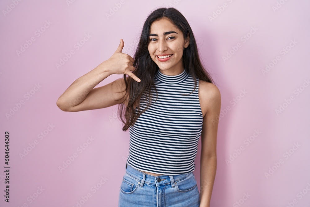 Young teenager girl wearing casual striped t shirt smiling doing phone gesture with hand and fingers like talking on the telephone. communicating concepts.