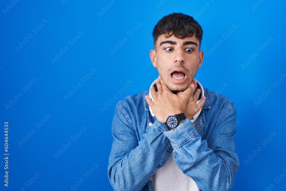 Young hispanic man standing over blue background shouting suffocate because painful strangle. health problem. asphyxiate and suicide concept. Young hispanic man standing over blue background shouting suffocate because painful strangle. health problem. asphyxiate and suicide concept.