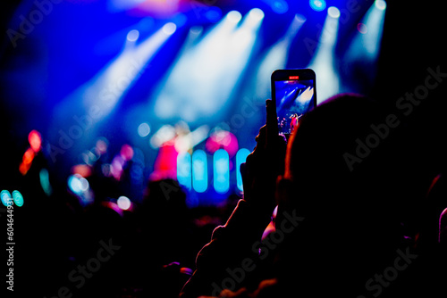 person taking photos with his cellphone oh a night life pop music concert 