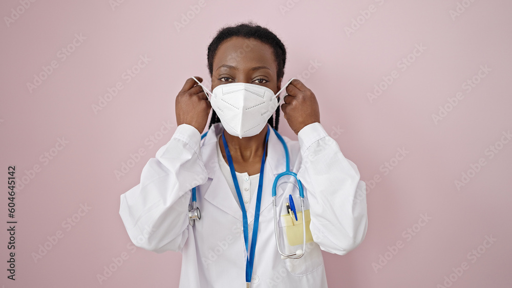 African american woman doctor wearing medical mask over isolated pink background