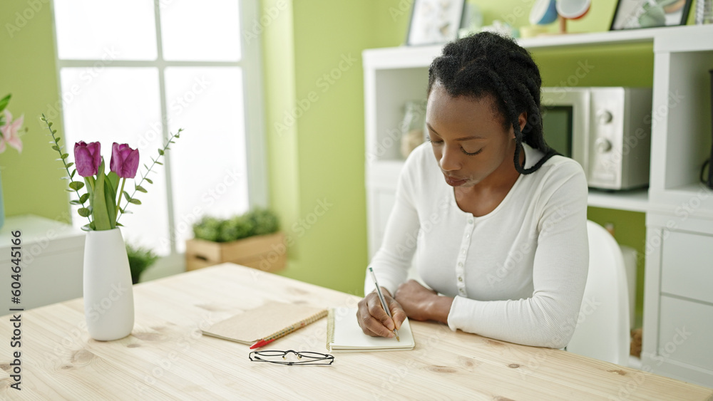 African american woman writing on notebook sitting on table at home African american woman writing on notebook sitting on table at home