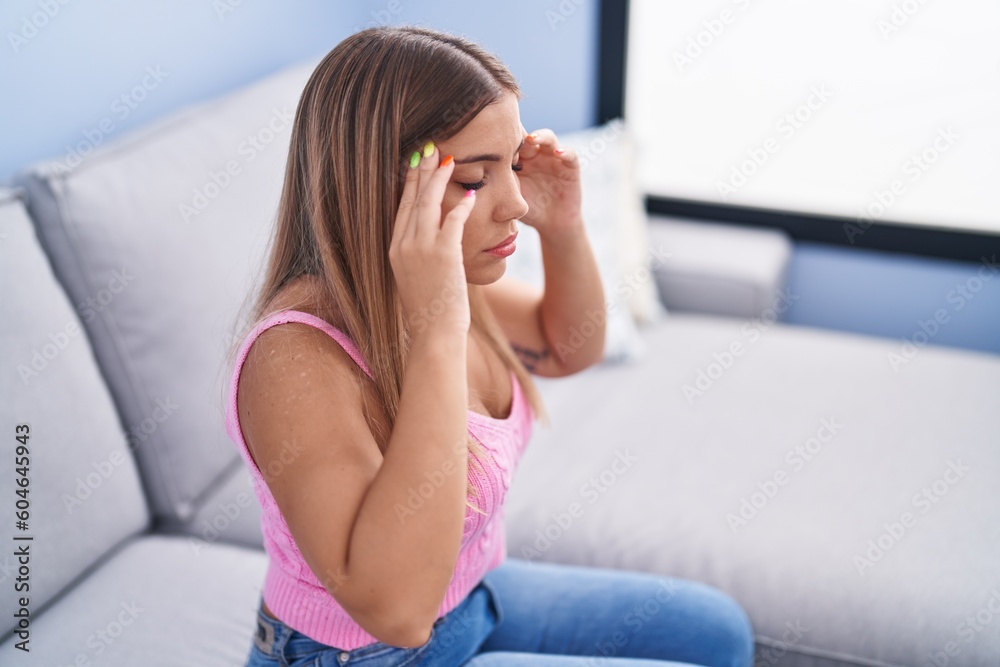 Young beautiful hispanic woman suffering for headache sitting on sofa at home Young beautiful hispanic woman suffering for headache sitting on sofa at home
