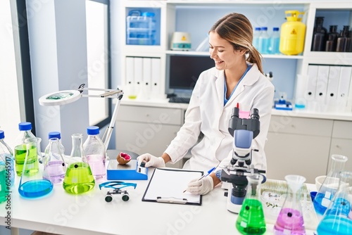 Young hispanic woman scientist weighing gemstone writing report at laboratory