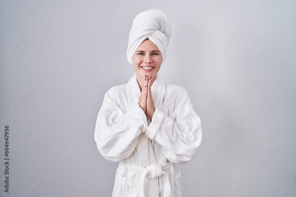 Blonde caucasian woman wearing bathrobe praying with hands together asking for forgiveness smiling confident. - obrazy, fototapety, plakaty 