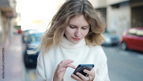 Young blonde woman using smartphone standing at street
