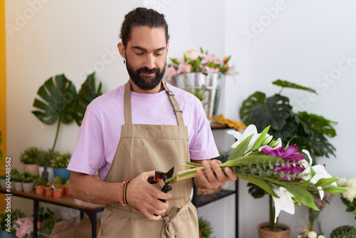 Young hispanic man florist cutting stem of flowers at flower shop