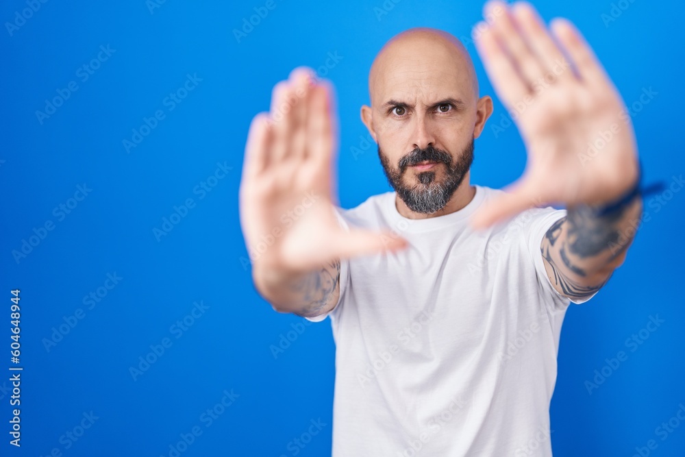 Hispanic man with tattoos standing over blue background doing frame using hands palms and fingers, camera perspective