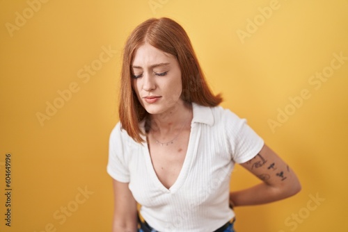 Young redhead woman standing over yellow background suffering of backache, touching back with hand, muscular pain