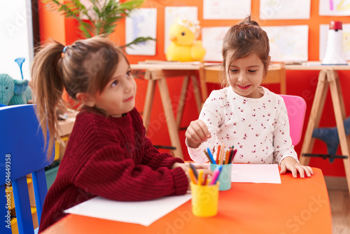 Adorable girls preschool students sitting on table drawing on paper at kindergarten