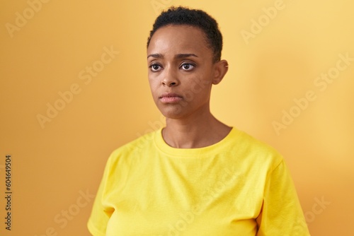 African american woman standing with serious expression over isolated yellow background © Krakenimages.com