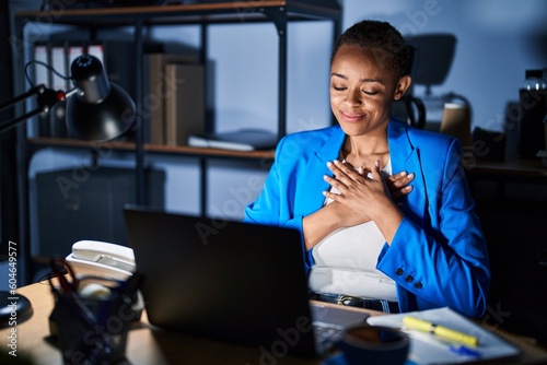Beautiful african american woman working at the office at night smiling with hands on chest with closed eyes and grateful gesture on face. health concept.