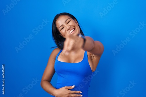 Hispanic woman standing over blue background laughing at you, pointing finger to the camera with hand over body, shame expression © Krakenimages.com