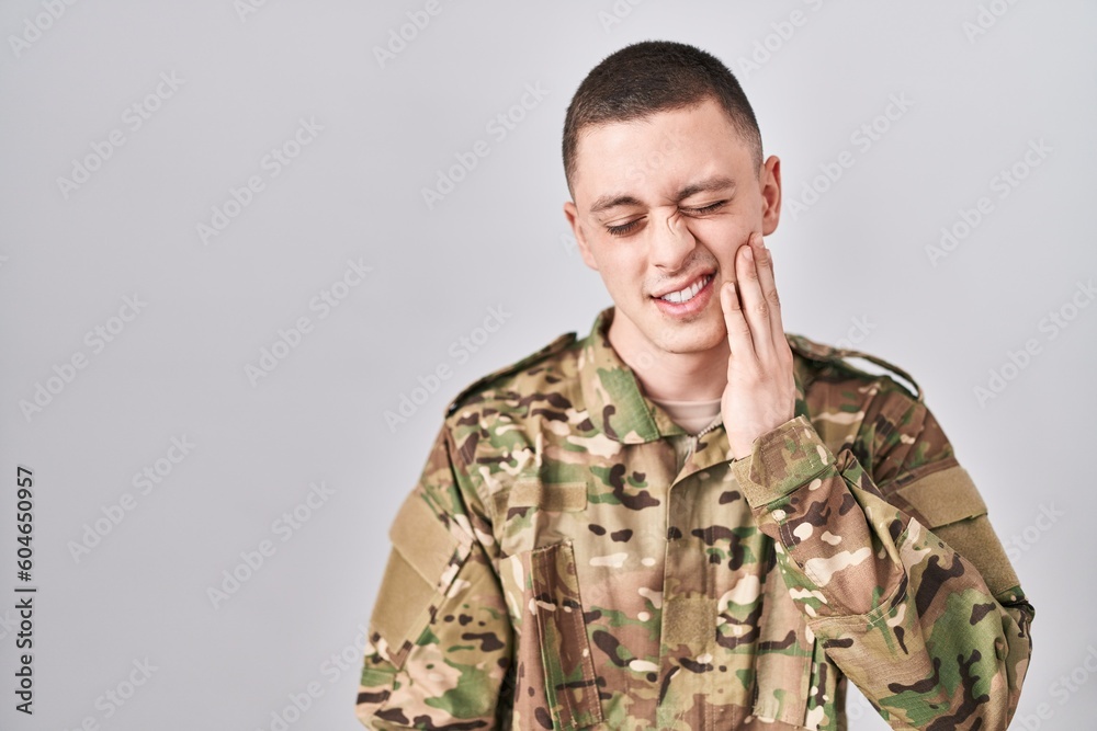 Young man wearing camouflage army uniform touching mouth with hand with painful expression because of toothache or dental illness on teeth. dentist