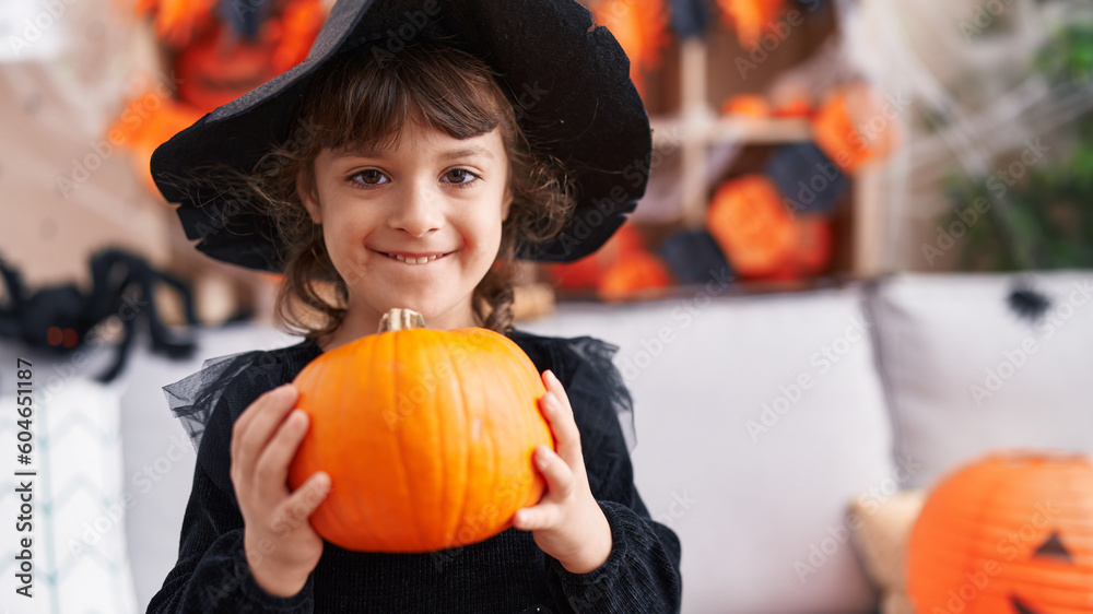Fototapeta premium Adorable hispanic girl having halloween party holding pumpkin at home