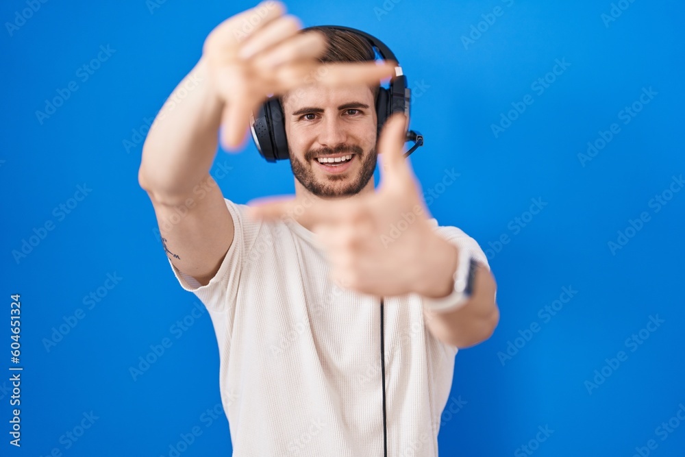 Naklejka premium Hispanic man with beard listening to music wearing headphones smiling making frame with hands and fingers with happy face. creativity and photography concept.