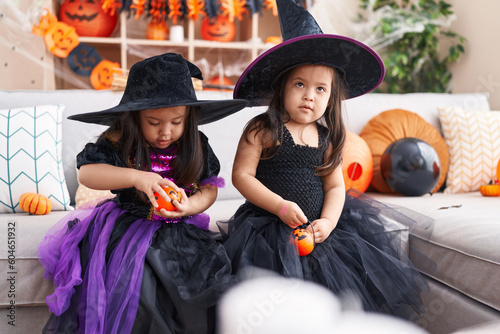 Adorable twin girls having halloween party holding pumpkin baskets at home