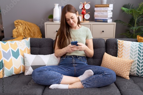 Young beautiful woman using smartphone sitting on sofa at home