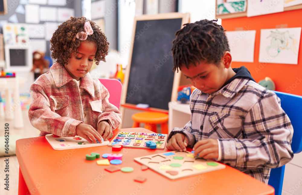 Adorable african american boy and girl playing with maths puzzle game sitting on table at kindergarten Adorable african american boy and girl playing with maths puzzle game sitting on table at kindergarten