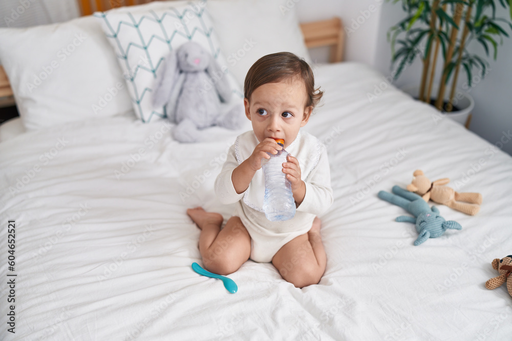 Adorable hispanic boy sitting on bed sucking bottle of water at bedroom Adorable hispanic boy sitting on bed sucking bottle of water at bedroom