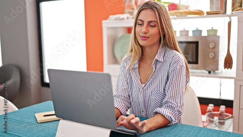 Young blonde woman using laptop sitting on table at dinning room