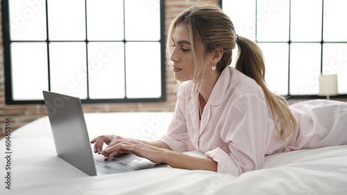 Young blonde woman using laptop lying on bed at bedroom