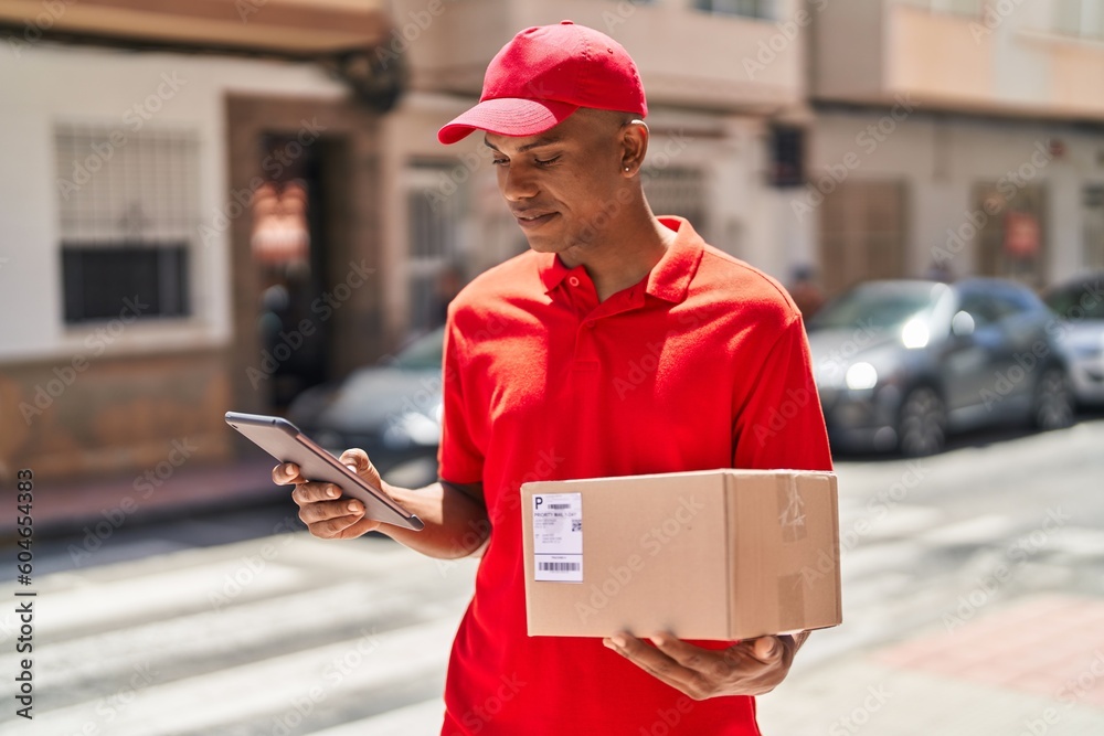 Young latin man delivery worker holding package using touchpad at street Young latin man delivery worker holding package using touchpad at street