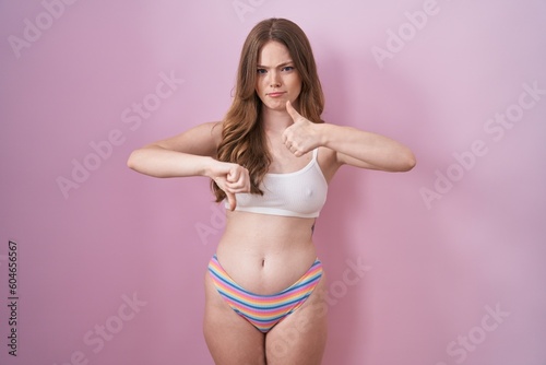 Caucasian woman wearing lingerie over pink background doing thumbs up and down, disagreement and agreement expression. crazy conflict