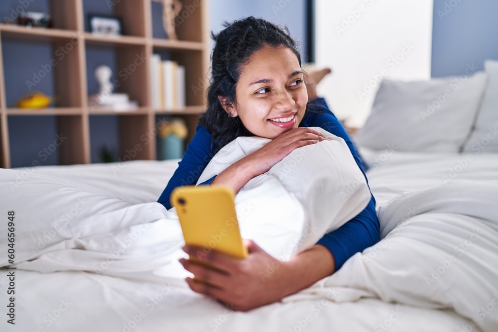Young latin woman using smartphone lying on bed at bedroom Young latin woman using smartphone lying on bed at bedroom