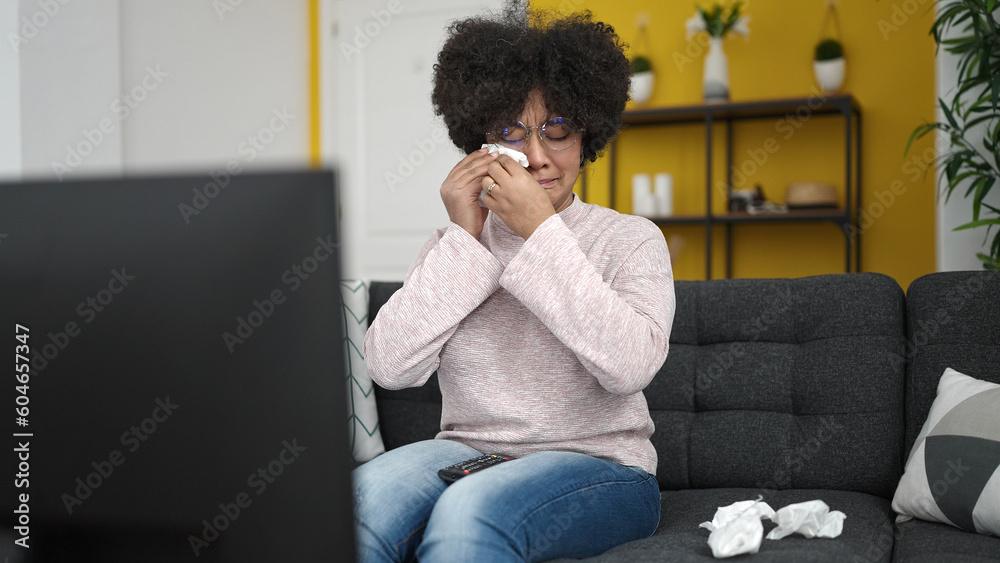 Young african american woman watching tv sitting on sofa at home Young african american woman watching tv sitting on sofa at home