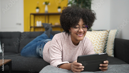 Young african american woman using touchpad lying on sofa at home