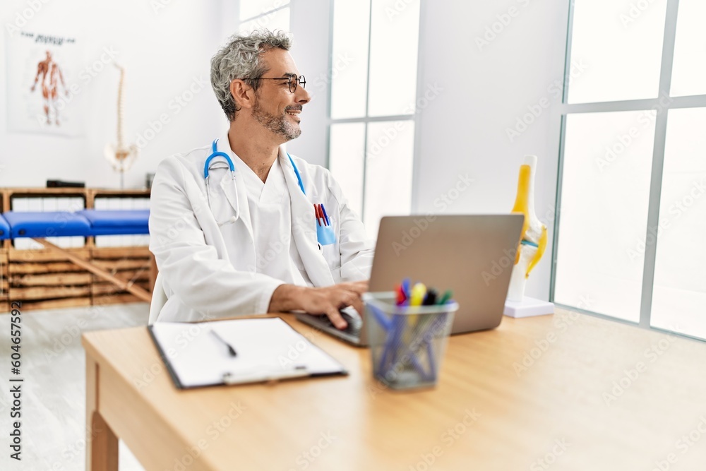 Middle age grey-haired man doctor using laptop working at rehab clinic