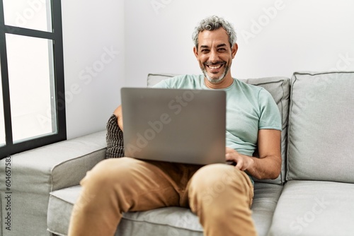 Middle age grey-haired man using laptop sitting on sofa at home