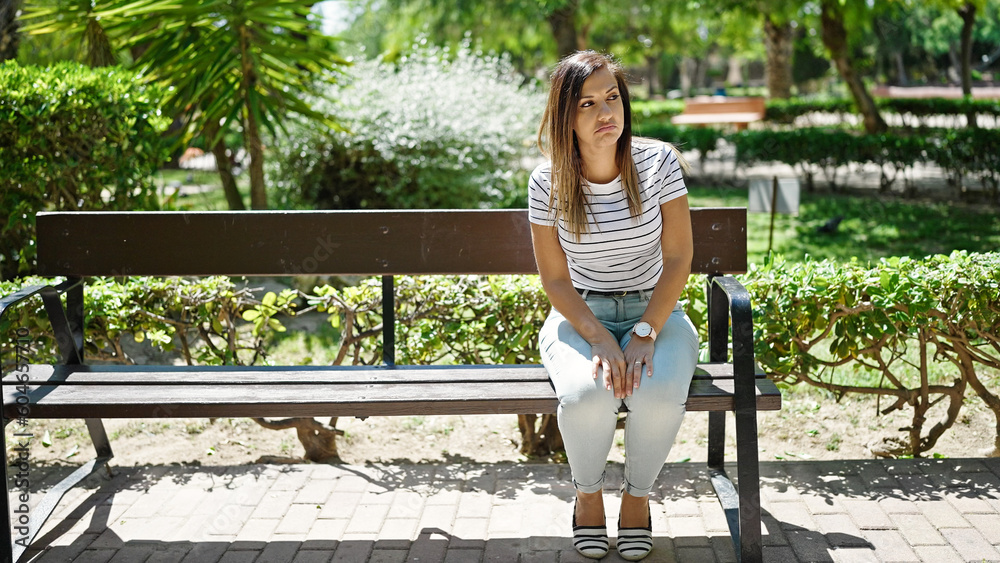 Middle eastern woman looking around with serious expression sitting on bench alone at street