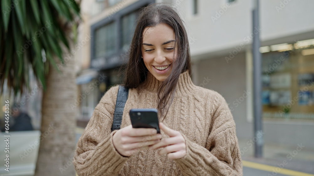 Young beautiful hispanic woman using smartphone smiling at street