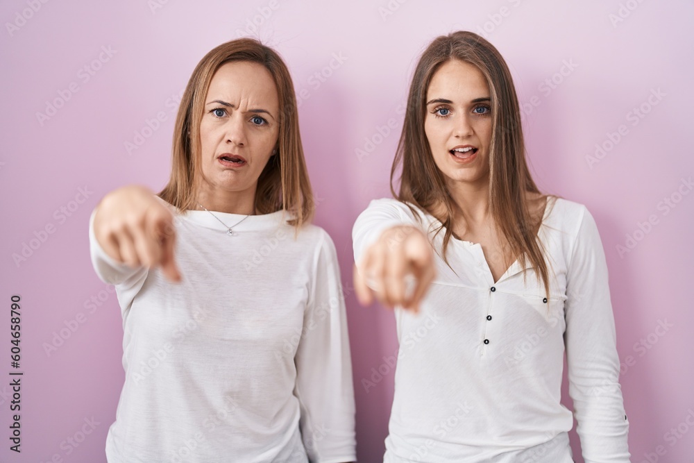 Middle age mother and young daughter standing over pink background pointing displeased and frustrated to the camera, angry and furious with you Middle age mother and young daughter standing over pink background pointing displeased and frustrated to the camera, angry and furious with you