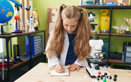 Adorable blonde girl student writing notes at laboratory classroom