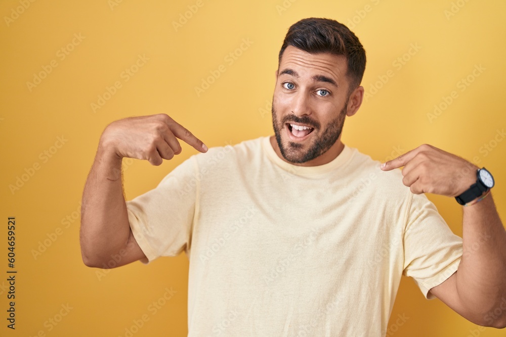 Handsome hispanic man standing over yellow background looking confident with smile on face, pointing oneself with fingers proud and happy. Handsome hispanic man standing over yellow background looking confident with smile on face, pointing oneself with fingers proud and happy.