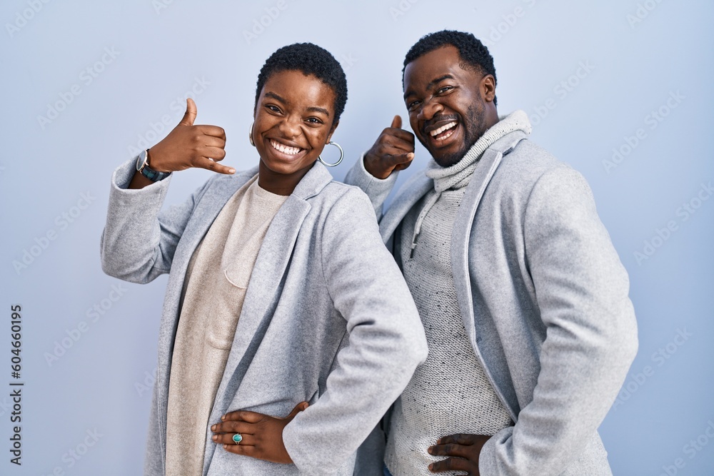 Young african american couple standing over blue background together smiling doing phone gesture with hand and fingers like talking on the telephone. communicating concepts. Young african american couple standing over blue background together smiling doing phone gesture with hand and fingers like talking on the telephone. communicating concepts.