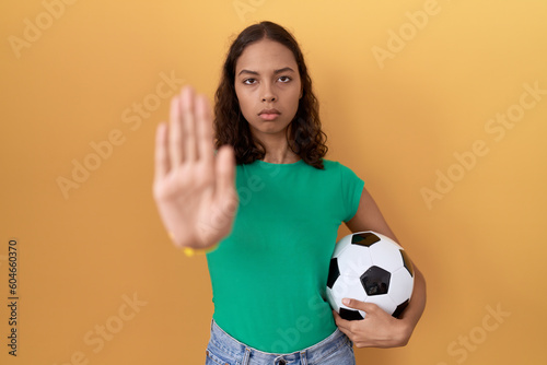 Young hispanic woman holding ball doing stop sing with palm of the hand. warning expression with negative and serious gesture on the face. © Krakenimages.com
