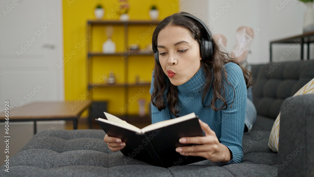 Young beautiful hispanic woman reading book lying on sofa wearing headphones at home Young beautiful hispanic woman reading book lying on sofa wearing headphones at home